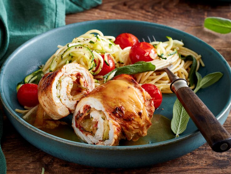 In einer Schüssel ist eine Portion Puten-Zucchini-Rouladen angerichtet. Sie wird mit Spagetti serviert.