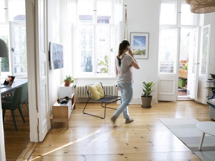 Frau läuft mit Telefon am Ohr in der Wohnung umher.