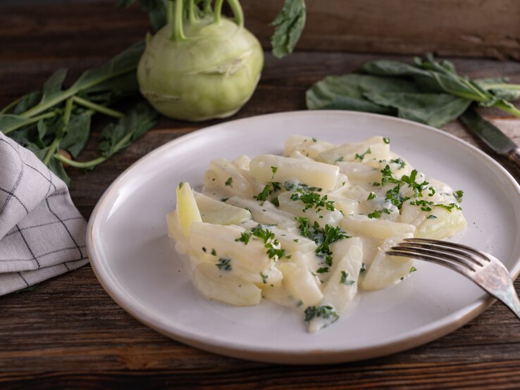 Weißer Teller belegt mit Rahmkohlrabi auf hölzernem Untergrund. 