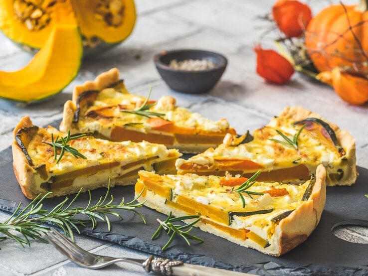 Vier Stücke Kürbis-Feta-Quiche auf einer schwarzen Schieferplatte.