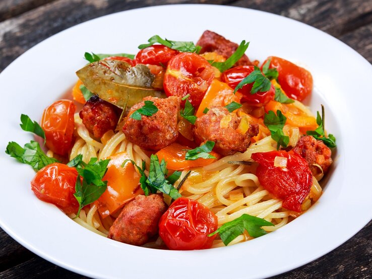 Ein weißer Teller mit dem Pastagericht auf dunklem Holzuntergrund.