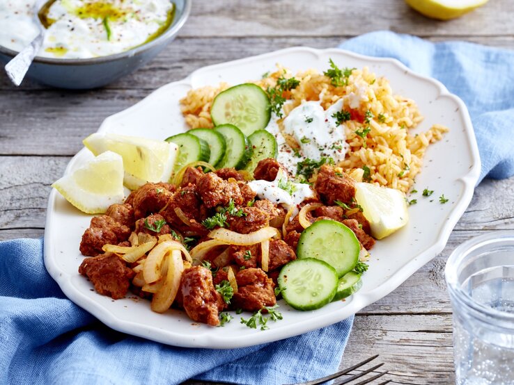 Auf einem Teller ist eine Veggie-Gyros-Platte mit Gurken, Zitrone und Reis angerichtet.