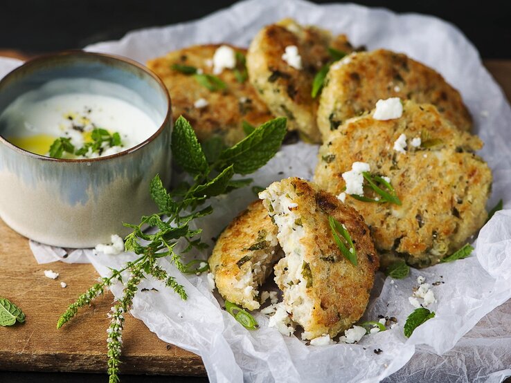 Saftige Bluhmenkohlfrikadellen mit Minzjoghurt, auf einem hellen Leinentuch serviert, bestreut mit Feta und frischer Minze. 