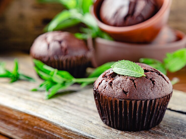 Frontal: drei Minz-Schoko-Muffins stehen auf eine Holzplatte.