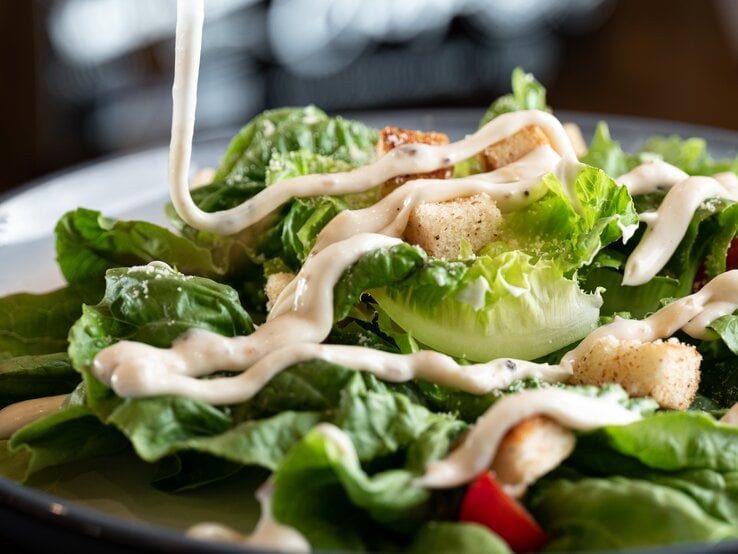 Dressing wird auf grünen Salat geträufelt. 