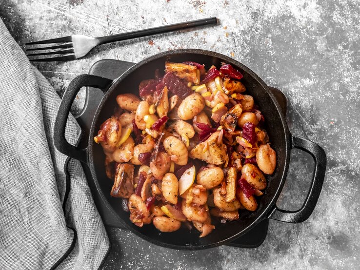 Gnocchi-Pfanne mit roter Bete, Huhn und Birne in gusseiserner Pfanne auf grauem Untergrund. 