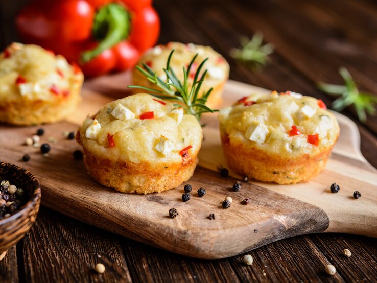 Feta-Muffins mit Paprika auf einem Holzschneidebrett neben einer Paprika