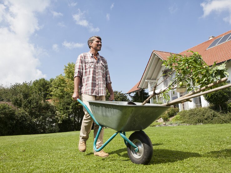 Ein Mann steht mit einer Schubkarre im Garten.