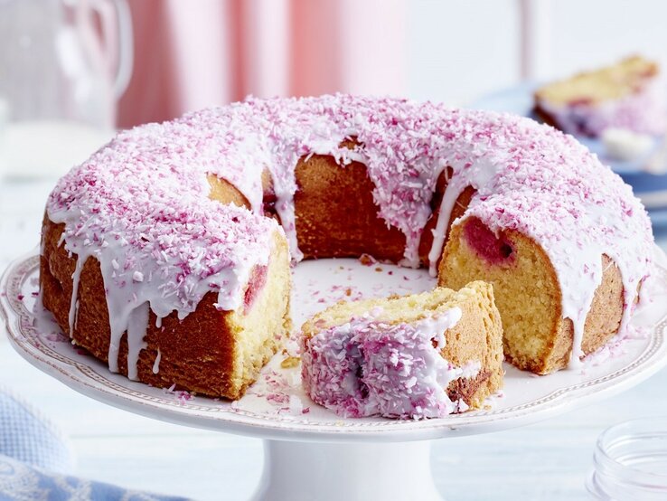 Auf einem Teller liegt ein Kokos-Himbeer-Kuchen. Er ist mit rosa Creme und Haferflocken dekoriert. 