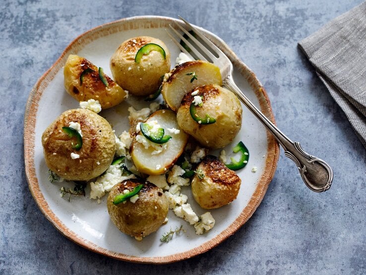 Teller auf hellblauem Untergrund belegt mit gebackenem Kohlrabi mit Feta. Daneben liegen eine Gabel und eine Serviette. 