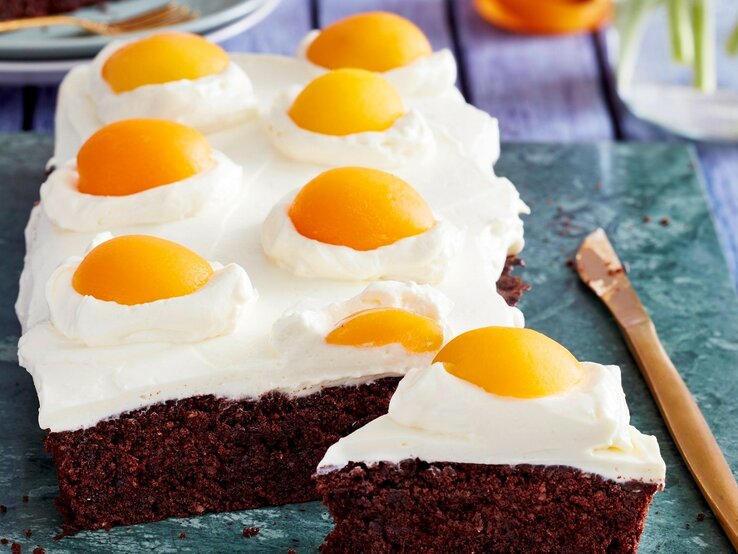 Auf einer Platte liegen Spiegeleier-Brownies. Sie sind mit Sprikosenhälften und einer Ricotta-Creme dekoriert und sehen aus wie aufgeschlagene Eier. 