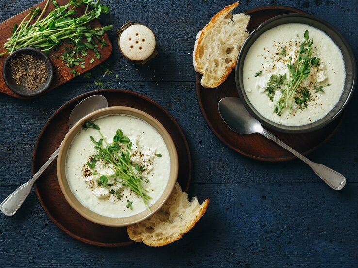 Blumenkohl-Feta-Suppe mit frischem Majoran belegt auf blauem Untergrund. 