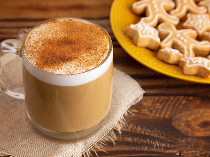 Eine Tasse mit Spekulatius-Latte auf einem Holztisch und einem gelben Teller im Hintergrund.