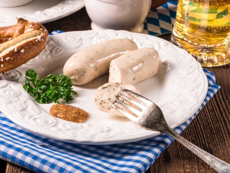 Ein Teller mit veganen Weiswürsten, süßem Senf und einer Brezel, daneben ein Glas Bier.