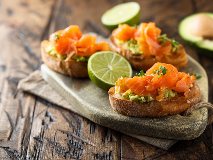 Drei Lachs-Bruschetta mit Avocado auf einem Holztablett.