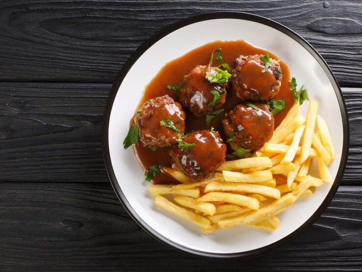 Lütticher Buletten und Pommes auf weißem Teller, angerichtet auf dunklem Holz. 