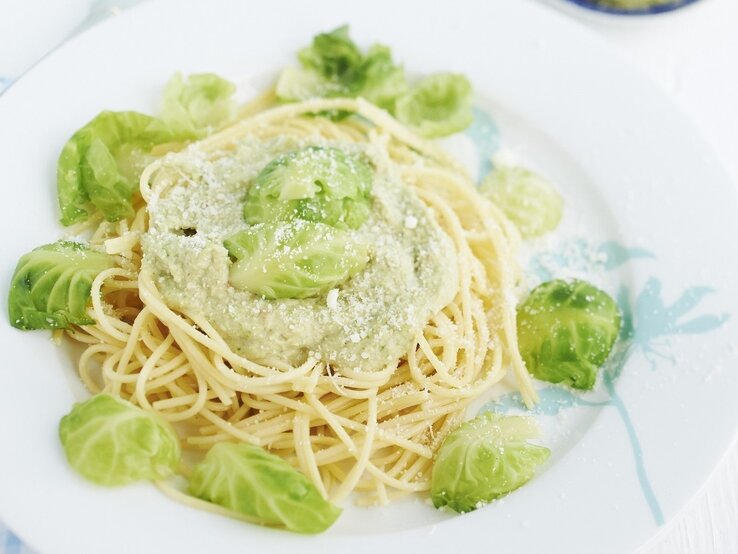 Spaghetti mit Rosenkohlpesto auf weißem Teller und hellem Untergrund. Draufsicht.