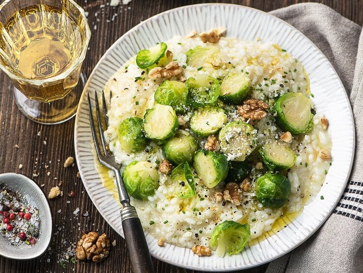 Ein Teller Rosenkohl-Risotto mit Walnüssen, daneben eine Gabel und ein Glas Wein.