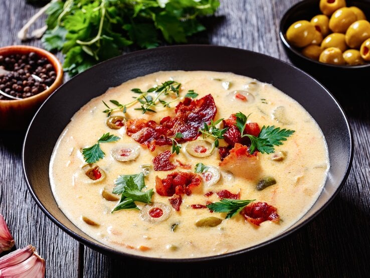 Käse-Bier-Suppe mit Bacon in schwarzer Schale auf schwarzem Holz. 