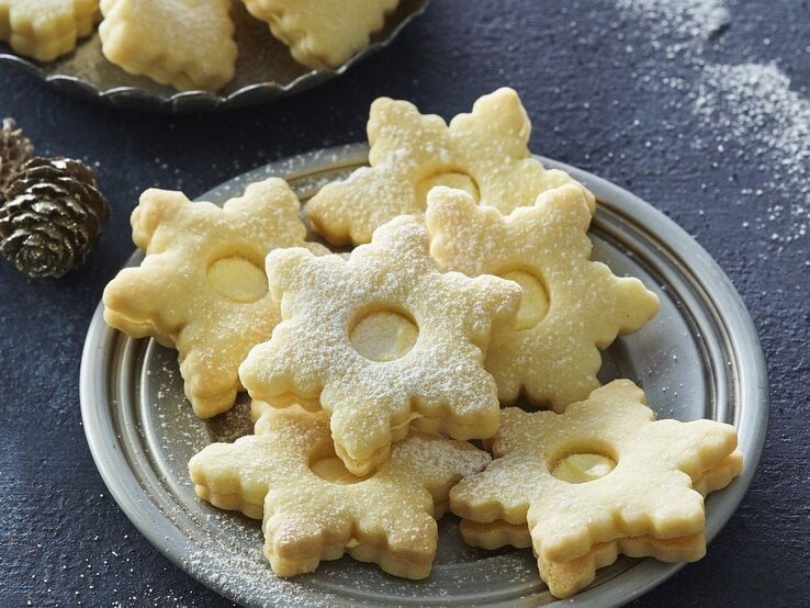 Auf einem Teller liegen Weihnachtsplätzchen mit Egg-Nogg-Creme. Sie sind mit Puderzucker bestreut.