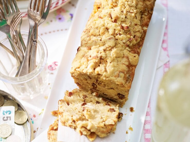 Apfel-Kastenkuchen mit Streuseln angeschnitten und serviert auf einem länglichen weißem Teller und hellem Untergrund.