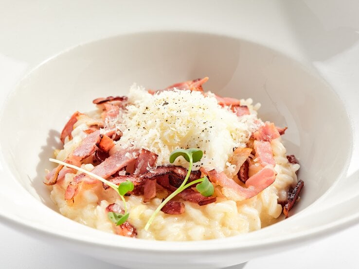 Risotto mit Speck und geriebenem Käse auf weißem Teller. 