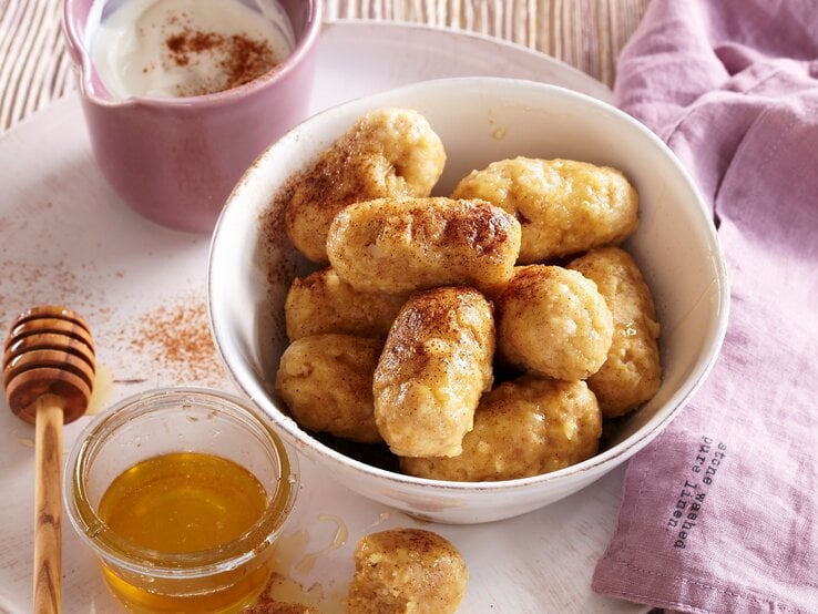 In einer weißen Schüssel liegen saftige Vanille-Apfel-Knödel. Sie sind mit Honig und Zimt verfeinert. 