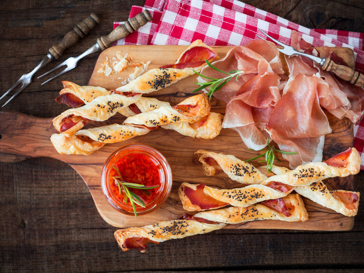 Kalorienarme Pizzastangen aus Skyr auf Holzbrett, daneben Parmaschinken und Gabeln