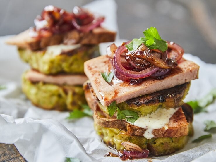 Knödelburger mit Leberkäse und roten Zwiebeln stehen auf Backpapier. 