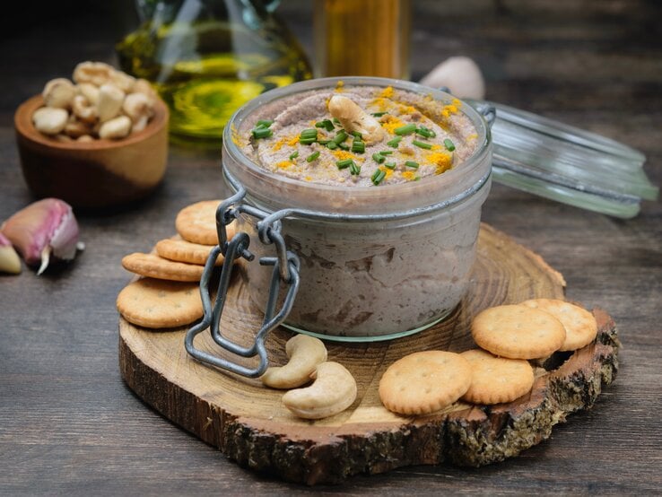 Ein Weckglas mit Cashew-Dressing und Schnittlauch, drumherum Cracker, Cashews, Knoblauch und eine Ölflasche.