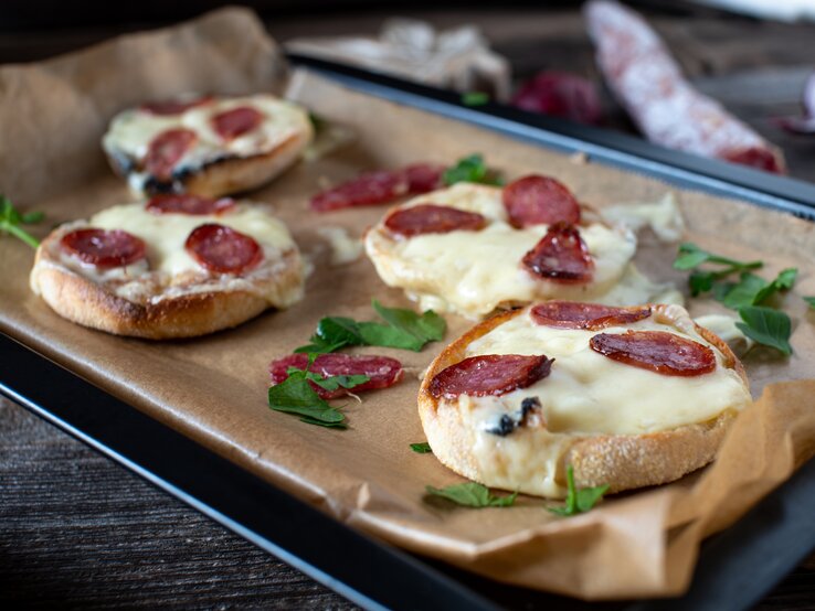 Ein mit Backpapier belegtes Blech mit Salami-Schmandbrötchen.