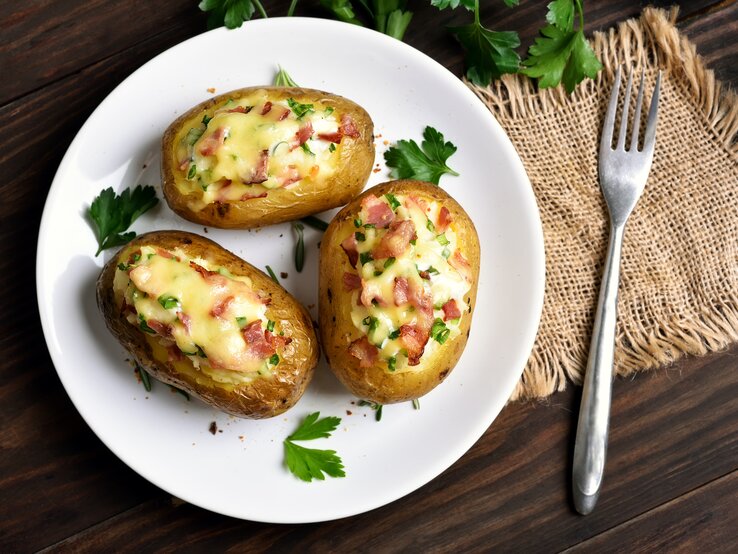 Gefüllte Kartoffeln mit Speck und Käse auf weißem Teller, angerichtet auf Holzuntergrund.