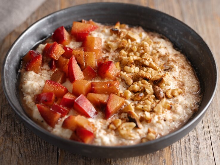 Eine schwarze Schüssel mit Walnuss-Pflaumen-Porridge auf einem Holztisch.