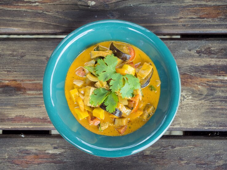 Ein grüner Teller mit würzigem Curry aus Gemüse und Koriander auf einem rustikalen Holztisch.