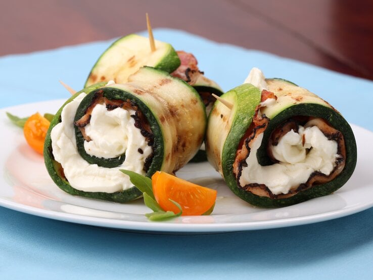 Zucchini-Schinken-Röllchen mit Mozzarella auf weißem Teller. 