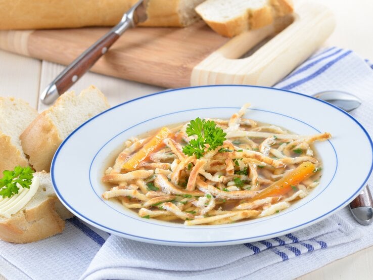 Blau-weißer Teller gefüllt mit Flädlesuppe auf einem blau-weißen Tuch. 