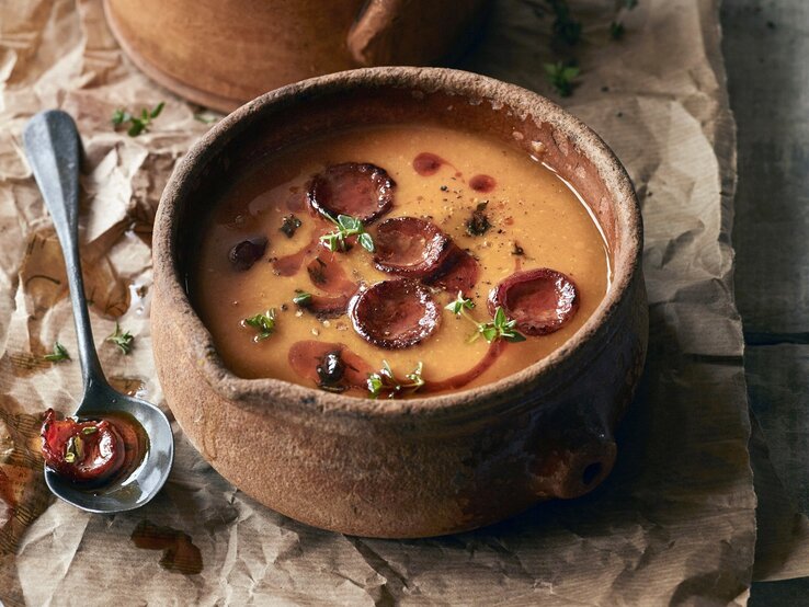 Rustikale Schale mit Kürbissuppe und gebratener Salami. 