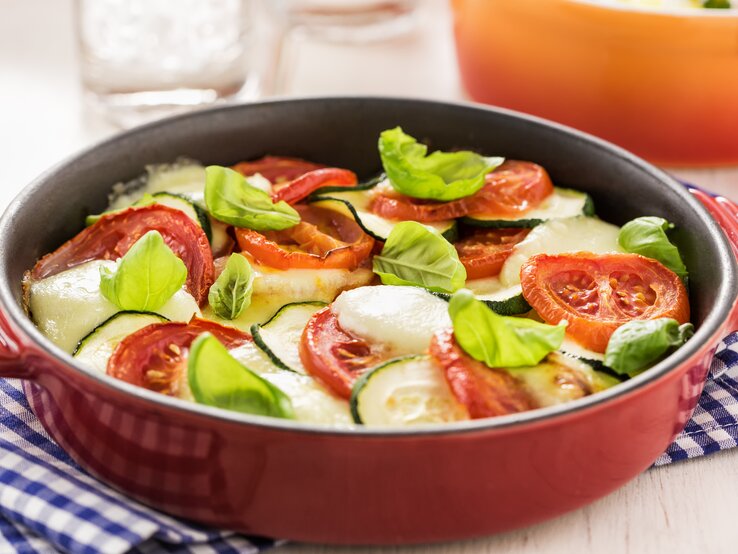 rote, runde Auflaufform gefüllt mit Zucchini, Tomate und Mozzarella.