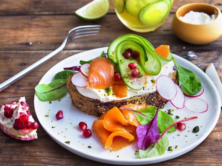 Draufsicht, schräg: Ein weißer Teller mit einer Low-Carb-Stulle mit Lachs und Pistazien.