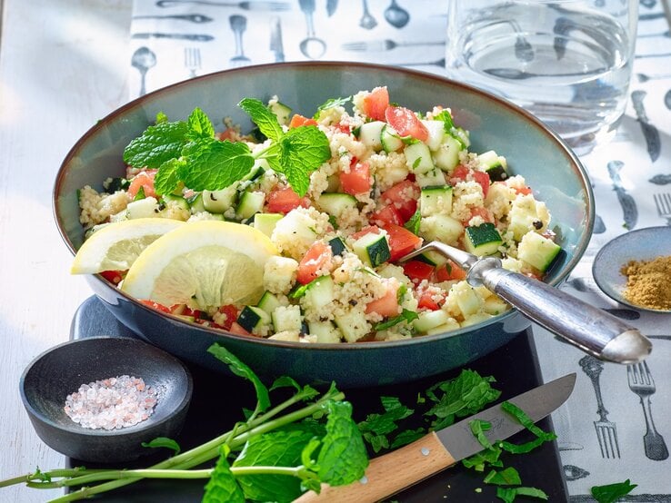 Couscous-Zucchini-Pfanne in einer blauen Schüssel. Auf dem Foto verteilt Salz, Gewürze, ein Messer und Wasser.