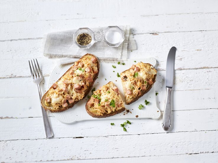 Ein weißer Holztisch mit den beiden belegten Brotscheiben von oben fotografiert.