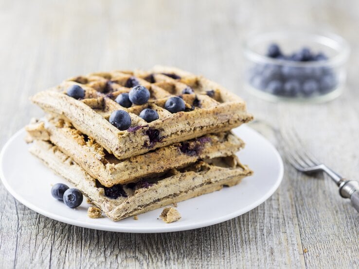 Mehrere Waffeln auf einem weißen Teller mit den Heidelbeeren von der Seite fotografiert.