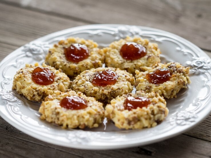 Mehrere Weihnachtsplätzchen "Husarenhüte" auf einem weißen, altmodischen Teller. 