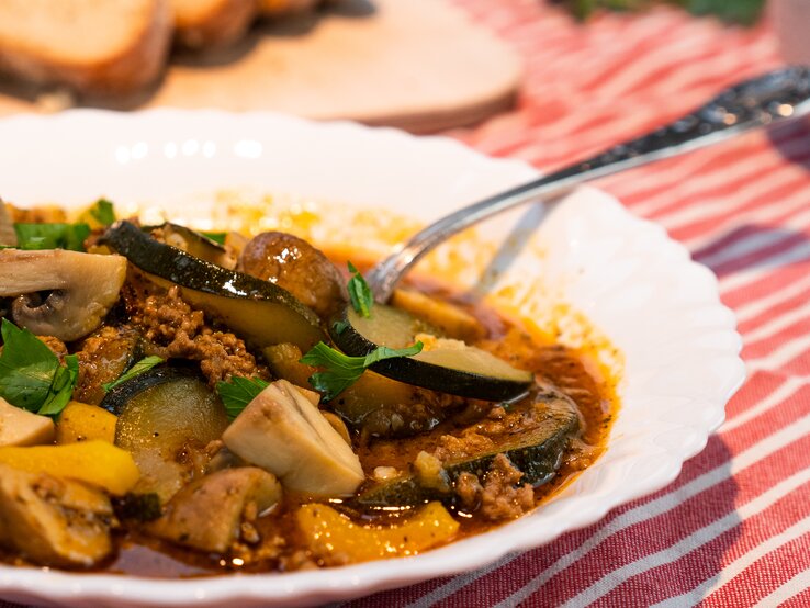 Weißer Teller gefüllt mit Bauerntopf mit Zucchini und Hackfleisch. 