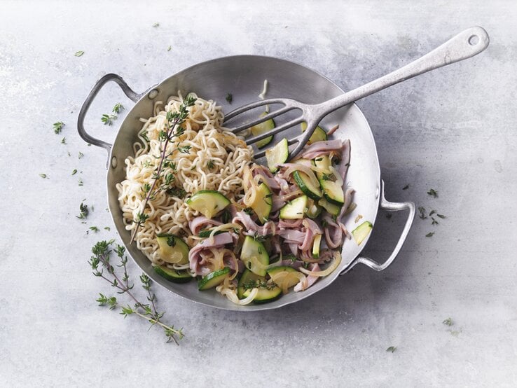 Ein silberner Wok mit dem Gericht auf einem grauen Steintisch direkt von oben fotografiert.