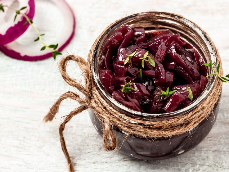 Auf einem hellen Untergrund steht ein Rote-Zwiebel-Aufstrich in einem Einweckglas. Darauf liegen zwei frische Thymianzweige.