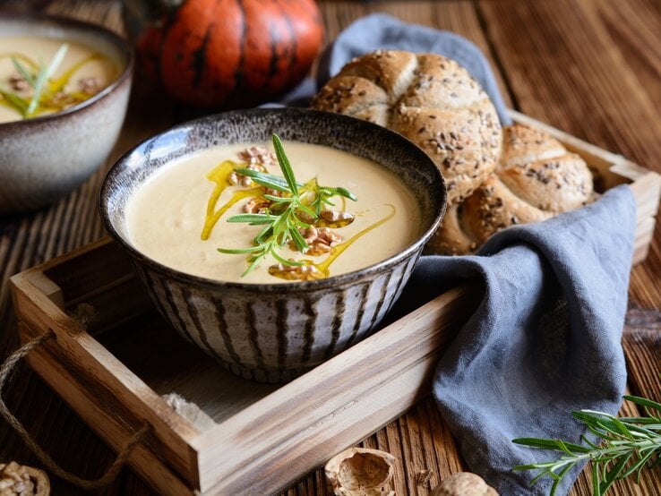 Eine Schüssel mit Walnuss-Kürbissuppe auf einem Holztablett.