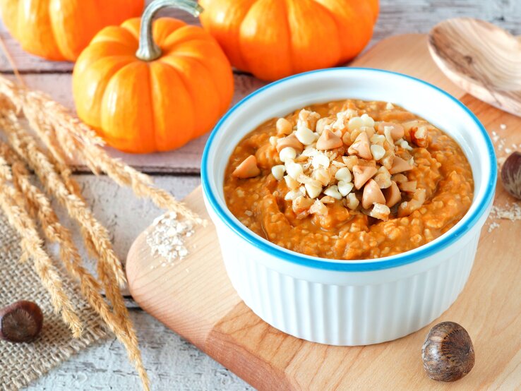 Eine weiß-blaue Schüssel mit Kürbis-Porridge auf einem Holzbrett.