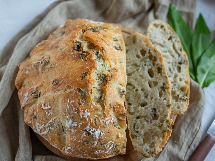 Bärlauchbrot mit Nüssen auf einem Geschirrtuch, daneben ein paar Bärlauchblätter.