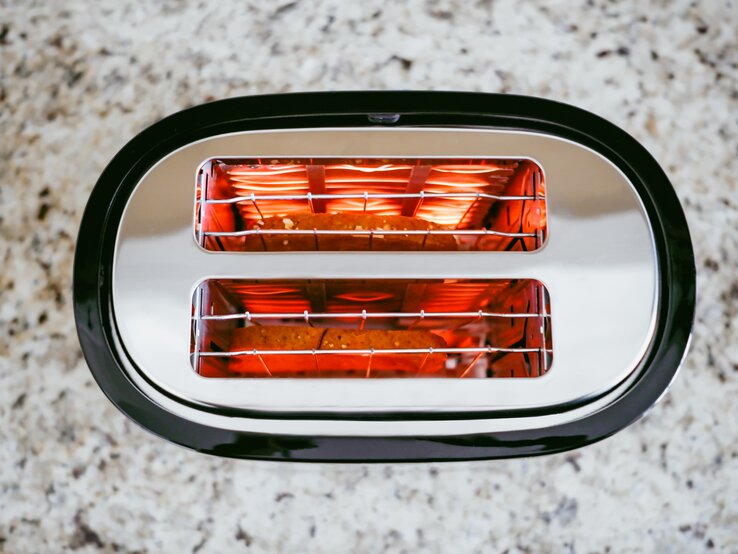 Oberansicht eines modernen Toasters. Die zwei Schlitze, aus denen das rotglühende Heizelement sichtbar ist, geben einen Einblick in die Funktionsweise des Geräts. | © Grace Cary / GettyImages